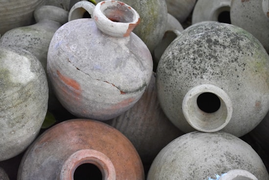 A collection of old, weathered clay pots with moss and cracks, arranged closely together. Each pot has a wide opening and varied textures that suggest aging and exposure to the elements.