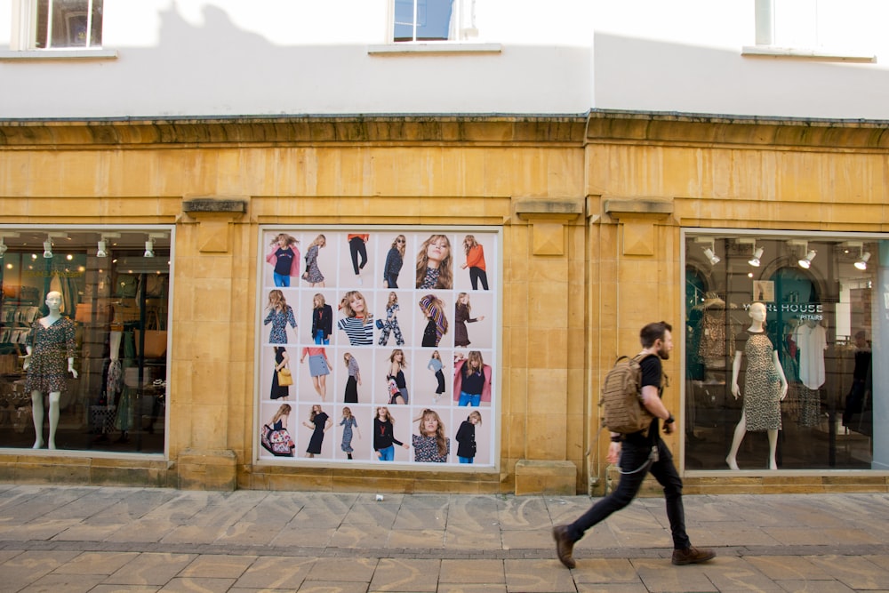 man carrying brown back walking pass boutique building during daytime