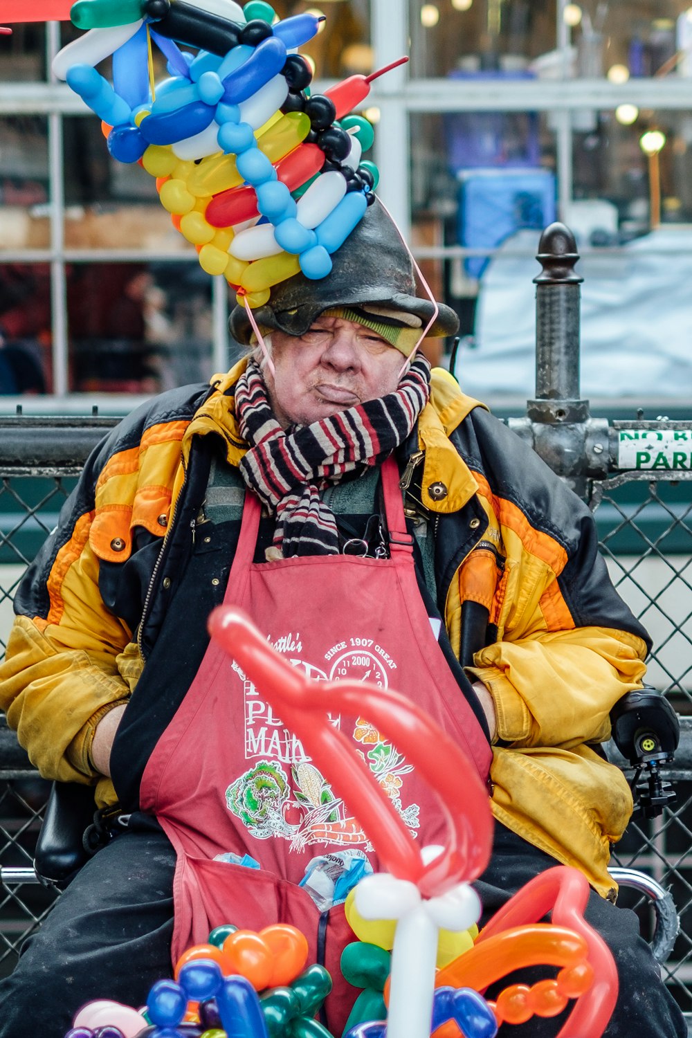 man sitting beside fence with balloon hat