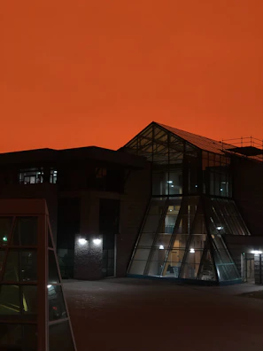 Evening exterior of a modern building glowing with vibrant golden-orange lighting against a dark sky.
