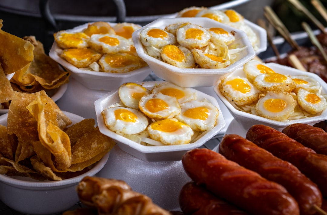 fried eggs, grilled hotdog on sticks, and fried chips on white bowls