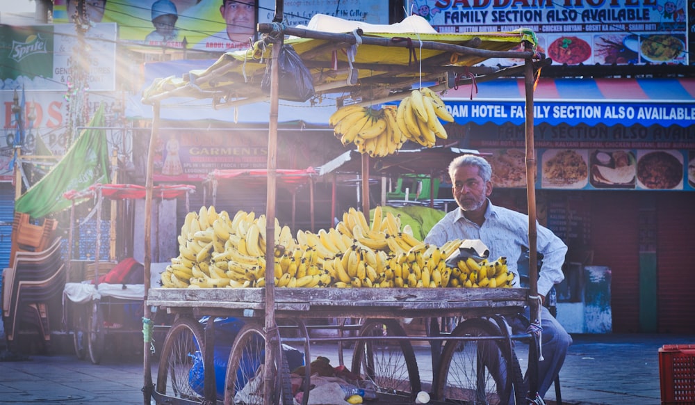 man sitting front of fruit stall at daytime