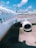A passenger airplane, identified by the 'SilkAir' logo, is parked on the tarmac at an airport. The view highlights the aircraft's exterior, including its windows and a jet engine. The background features airport facilities and clear blue skies with scattered clouds.