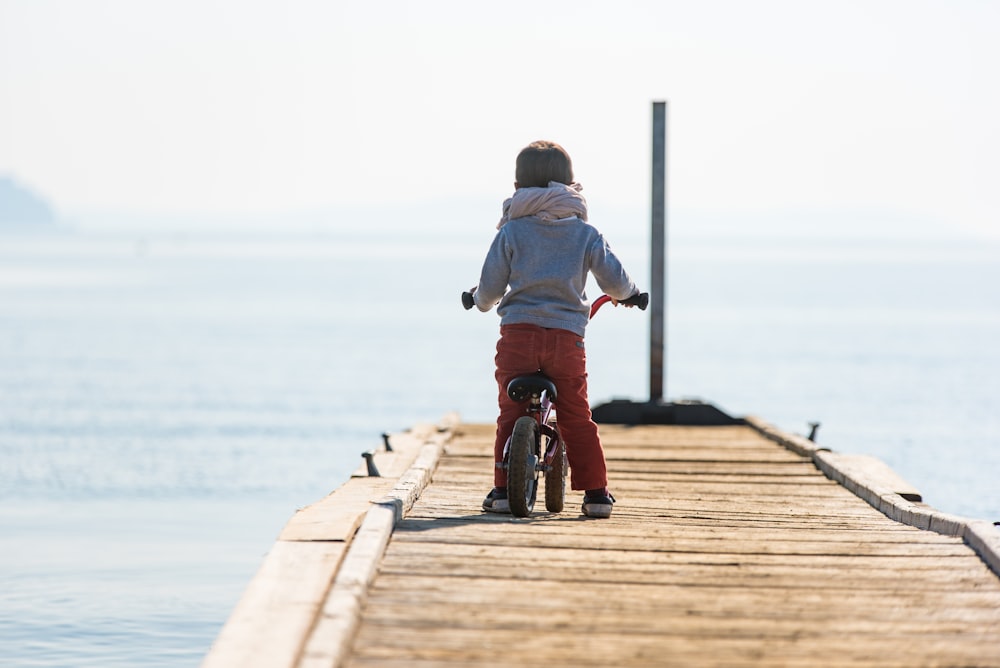 toddler wearing white scarf riding bicycle on brown dockl