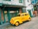 A vintage yellow taxi with the text 'Yellow Cab Co.' on the side is parked on a wooden street in front of a building with green trim and large windows. The scene has a nostalgic feel, with elements reminiscent of a bygone era.
