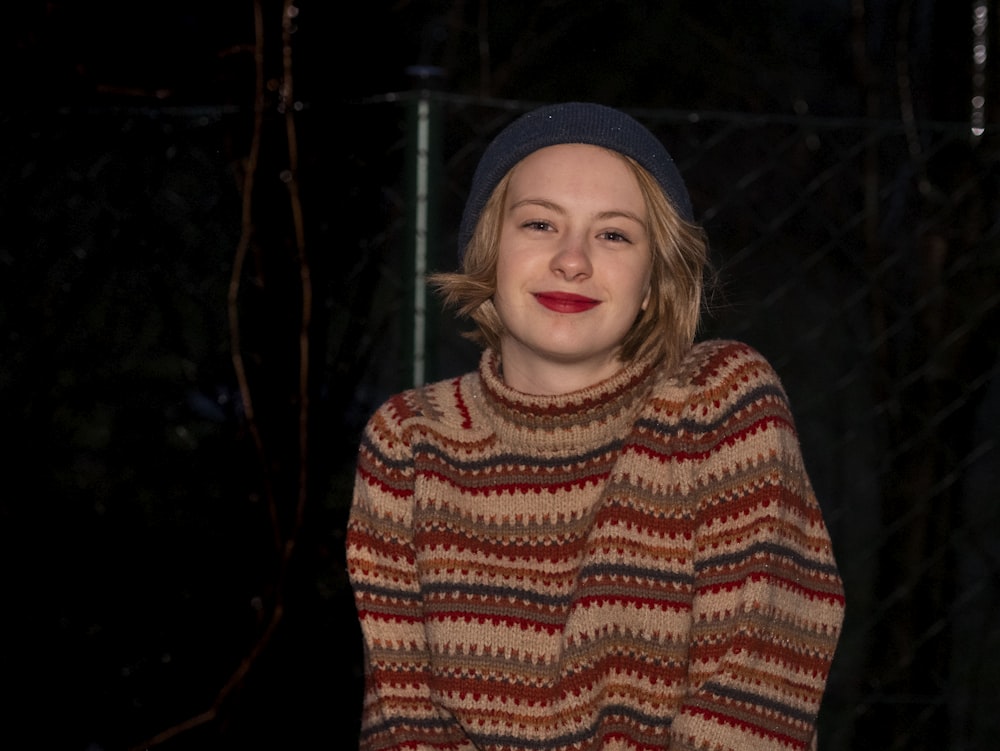 smiling woman standing while wearing red and brown sweater