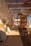 A cozy outdoor seating area lined with cushions and pillows in various patterns and colors. The area is shaded by a wooden pergola with a woven cover, casting intricate shadows. Natural materials and soft lighting create a warm and inviting atmosphere.