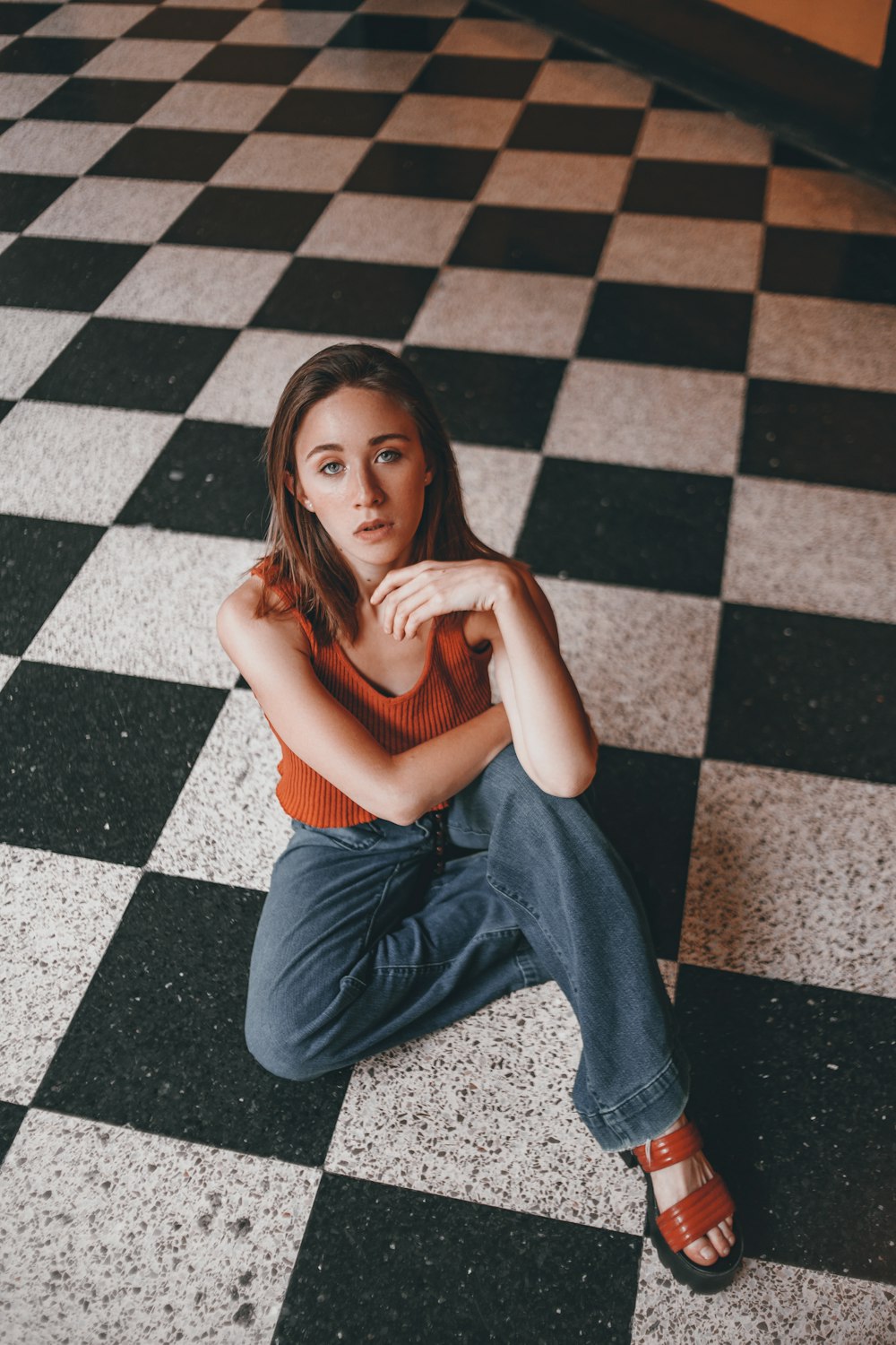 femme en débardeur marron et jeans bleus assis sur le sol