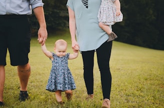couple holding baby's arm walking on grass field