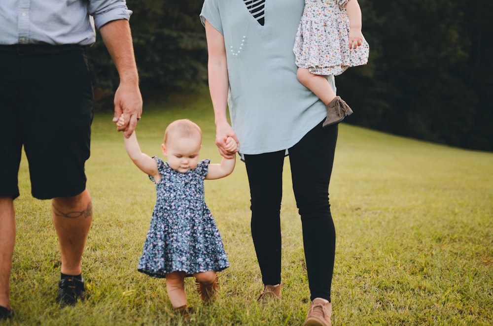 couple holding baby's arm walking on grass field