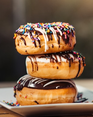 three stacked chocolate-coated donuts with colorful sprinkles