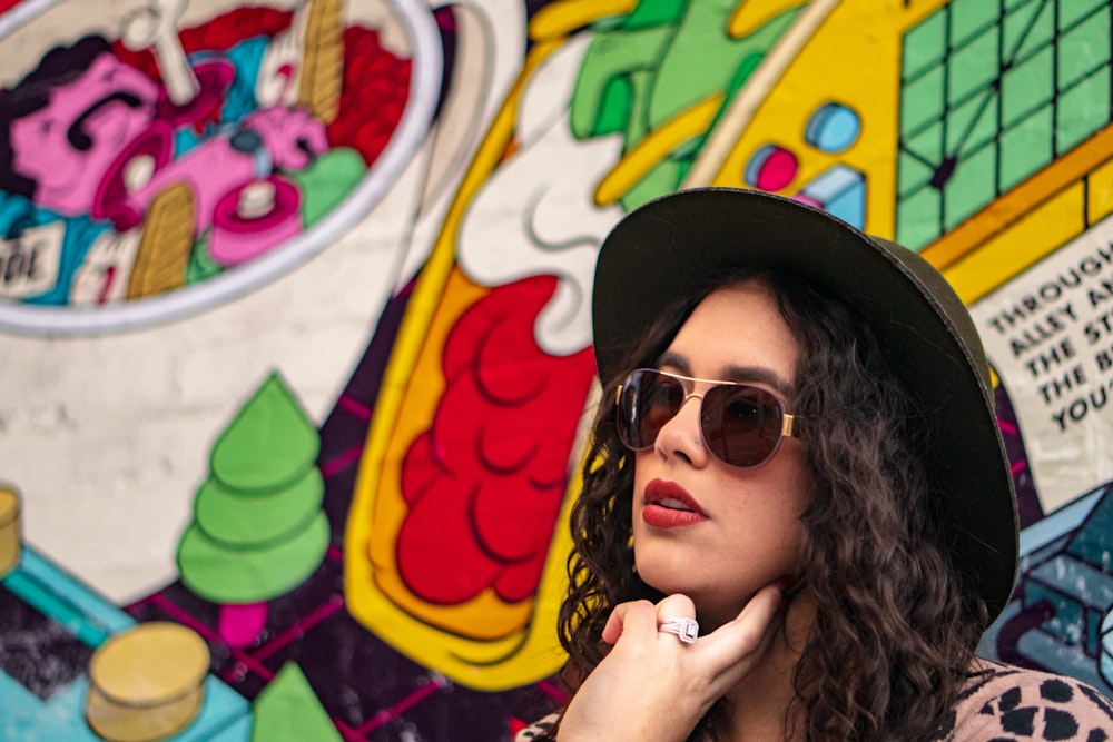 Mujer con gafas de sol negras y sombrero al lado de graffiti