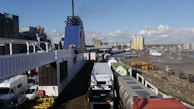 A busy warehouse dock with trucks being loaded under a clear sky.