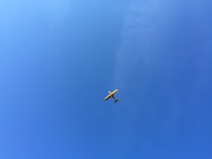 A young pilot confidently taking off in a light aircraft against a clear blue sky.