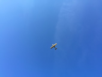 A small light aircraft flying high in a clear blue sky with no visible clouds.