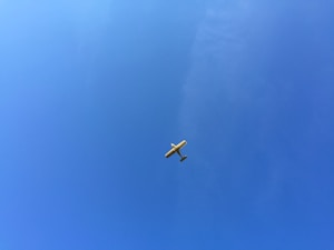 A small light aircraft flying high in a clear blue sky with no visible clouds.