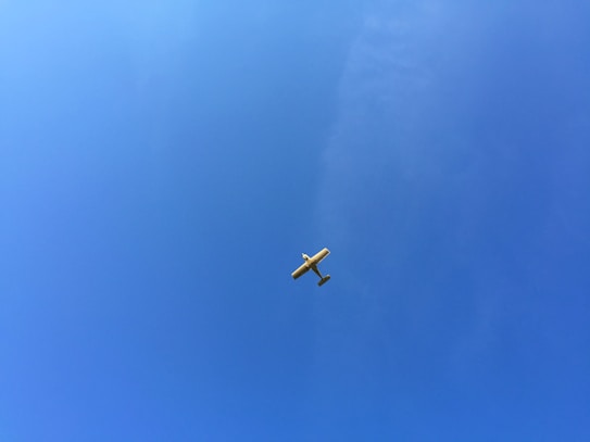 A small light aircraft flying high in a clear blue sky with no visible clouds.