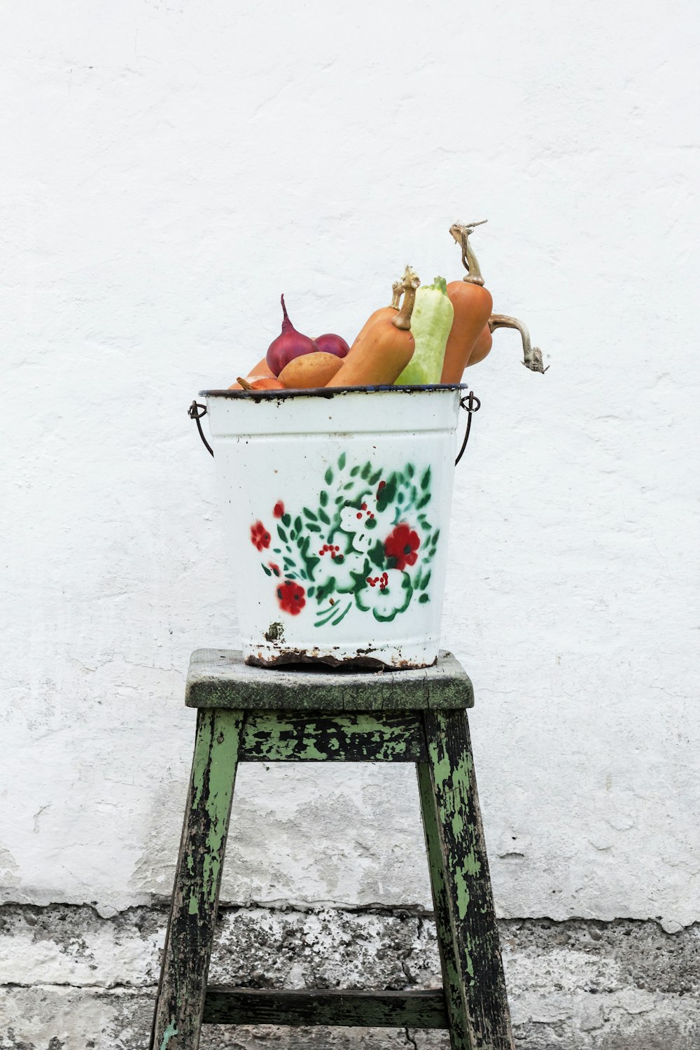 vegetais em balde floral branco e multicolorido no banquinho de madeira verde