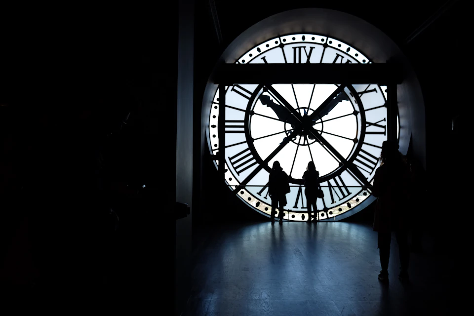 Large clock with Roman numerals dominates indoor space, casting a shadow on right wall