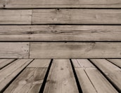 Wooden planks with visible grain patterns and some knots, arranged horizontally and vertically. The wood has a weathered appearance, with natural imperfections and variations in color.