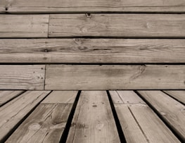 Wooden planks with visible grain patterns and some knots, arranged horizontally and vertically. The wood has a weathered appearance, with natural imperfections and variations in color.