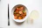 A vibrant bowl of steaming Asian noodles with fresh vegetables and chopsticks.