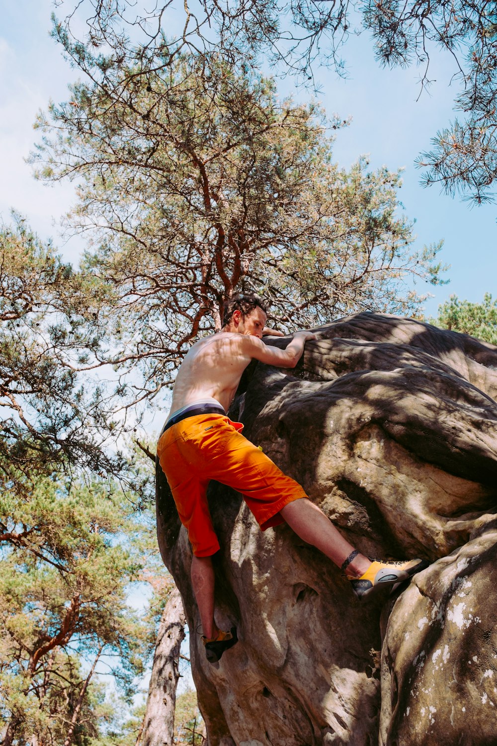 topless man climbing on big rock during daytime