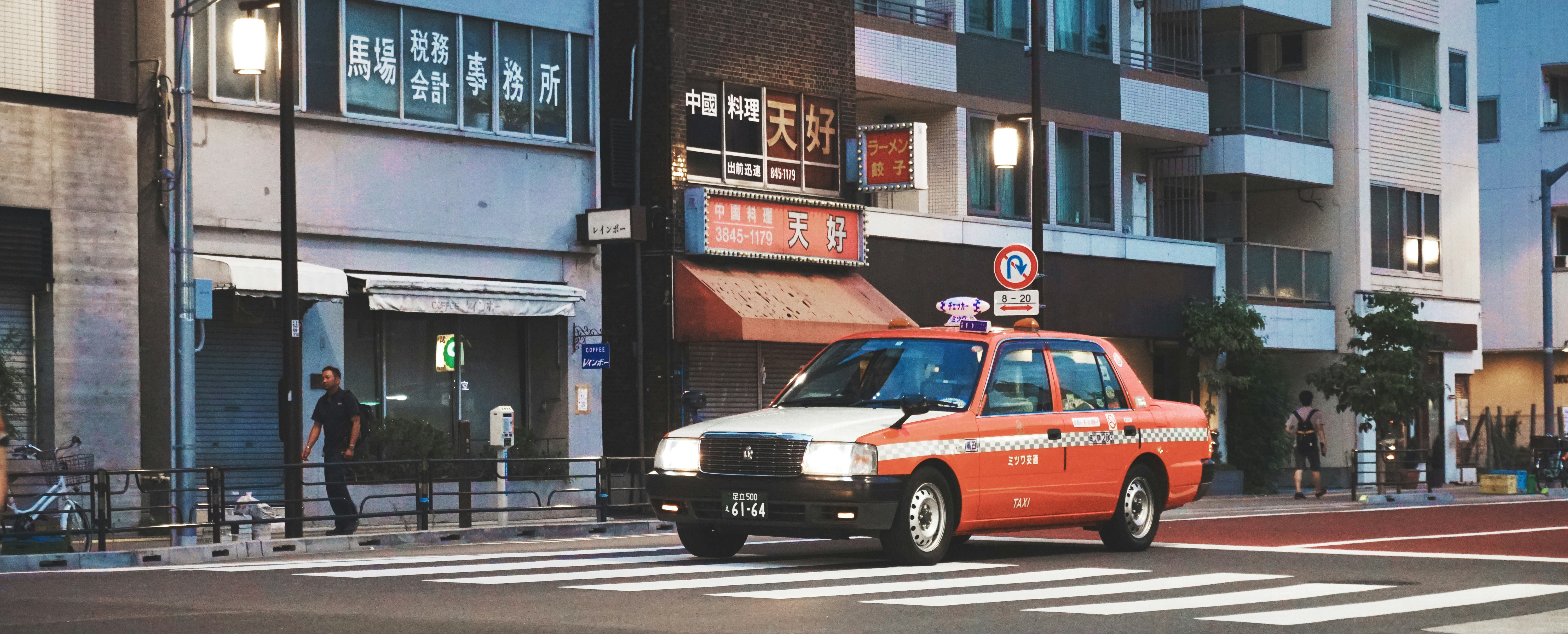 orange sedan at road beside gray building