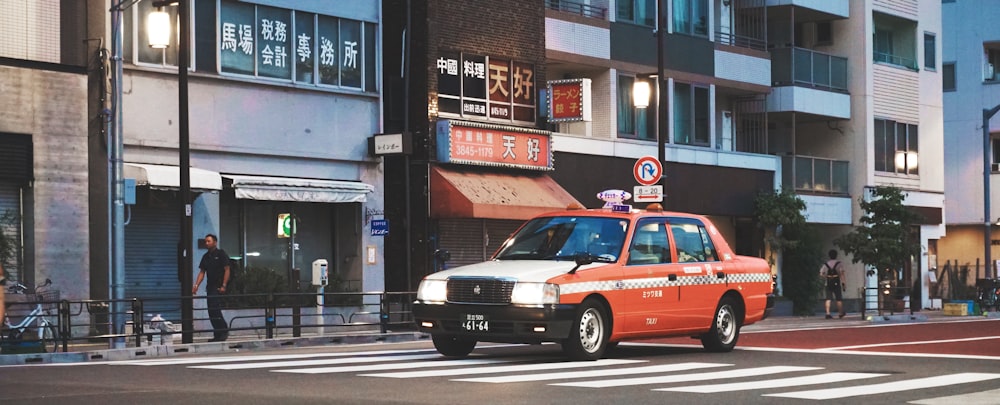 orange sedan at road beside gray building