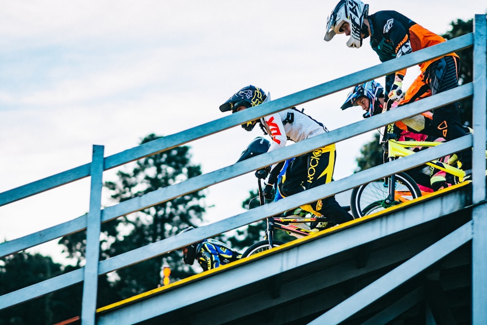 low-angle photography of several bicycle riders passing beside white guardrail during daytime