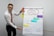A man wearing glasses, a white shirt, and an orange tie is standing beside a flip chart. The flip chart displays the 'SQ3R-Methode' with the words Survey, Question, Read, Recite, and Review highlighted on different colored paper. The background is plain, and there are additional colored circles partially visible on the wall.