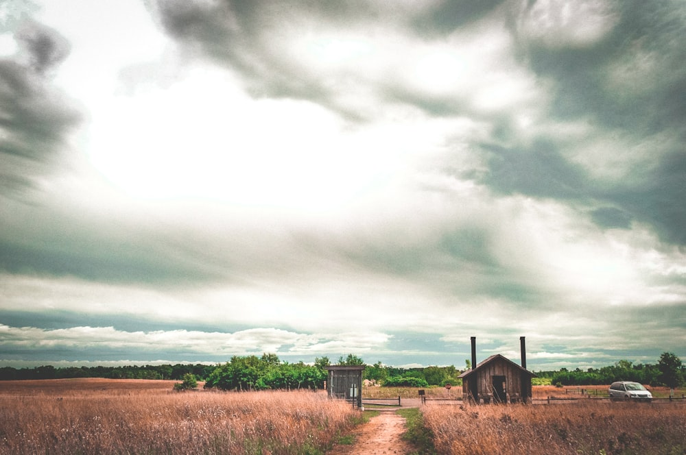 barn house and vehicle in middle of open field under cloudy sky