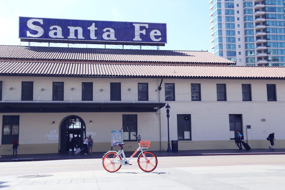 bicicletta bianca e arancione parcheggiata di fronte all'edificio di Santa Fe durante il giorno