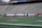 A group of athletes dressed in white and red uniforms stand in a line on a sports field, likely preparing for a game. They are being photographed by several people, while the empty bleachers in the background suggest an upcoming event.