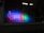 A brightly lit LED sign displays the word 'OPEN' in red, blue, and green colors. The lights are shining through a fogged-up window, indicating a warm atmosphere inside against a cooler exterior.