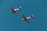 Two vintage military aircraft fly in formation against a clear blue sky. The planes feature distinctive red stars and numbers on their wings and fuselage, indicative of their historical Soviet origin.