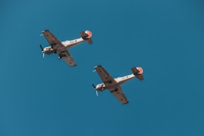 Two vintage military aircraft fly in formation against a clear blue sky. The planes feature distinctive red stars and numbers on their wings and fuselage, indicative of their historical Soviet origin.