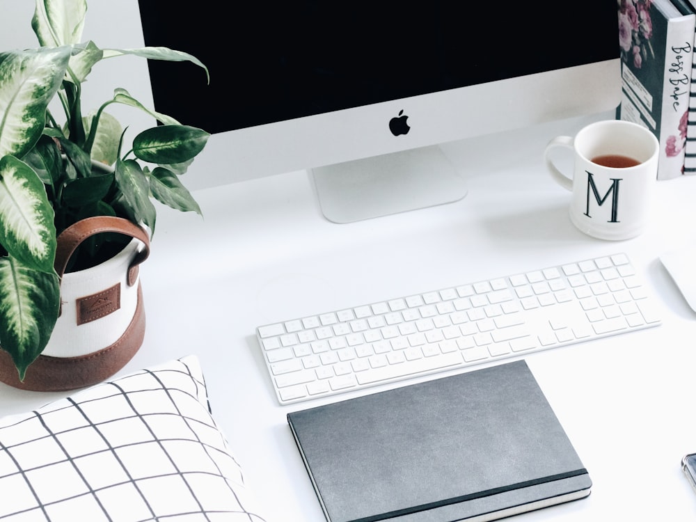 white M ceramic mug near iMac monitor