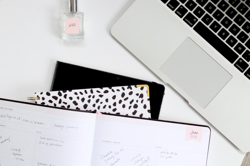 MacBook near fragrance bottle on white surface