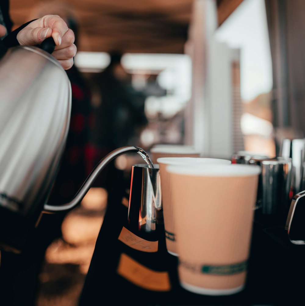 foto con messa a fuoco superficiale di persona che versa liquido su tazza marrone