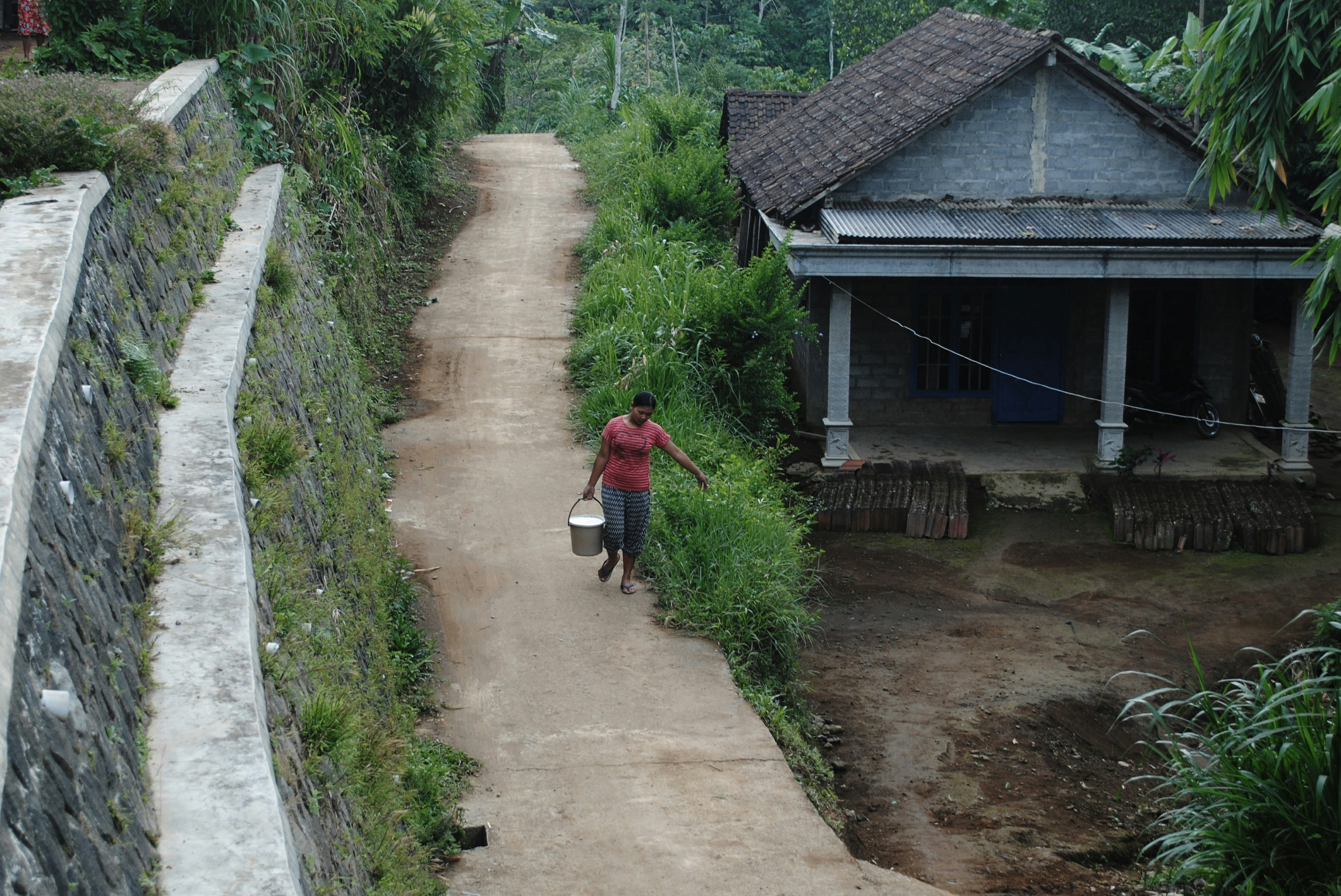 woman holding white pail while walking on road during daytime
