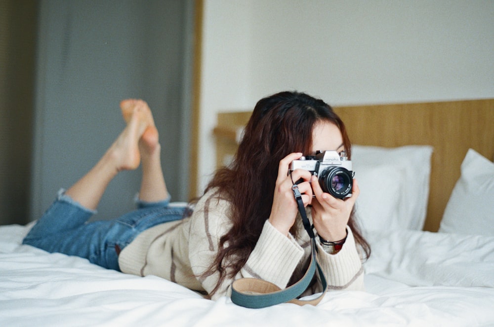 SLR 카메라로 사진을 찍는 침대에 있는 여자