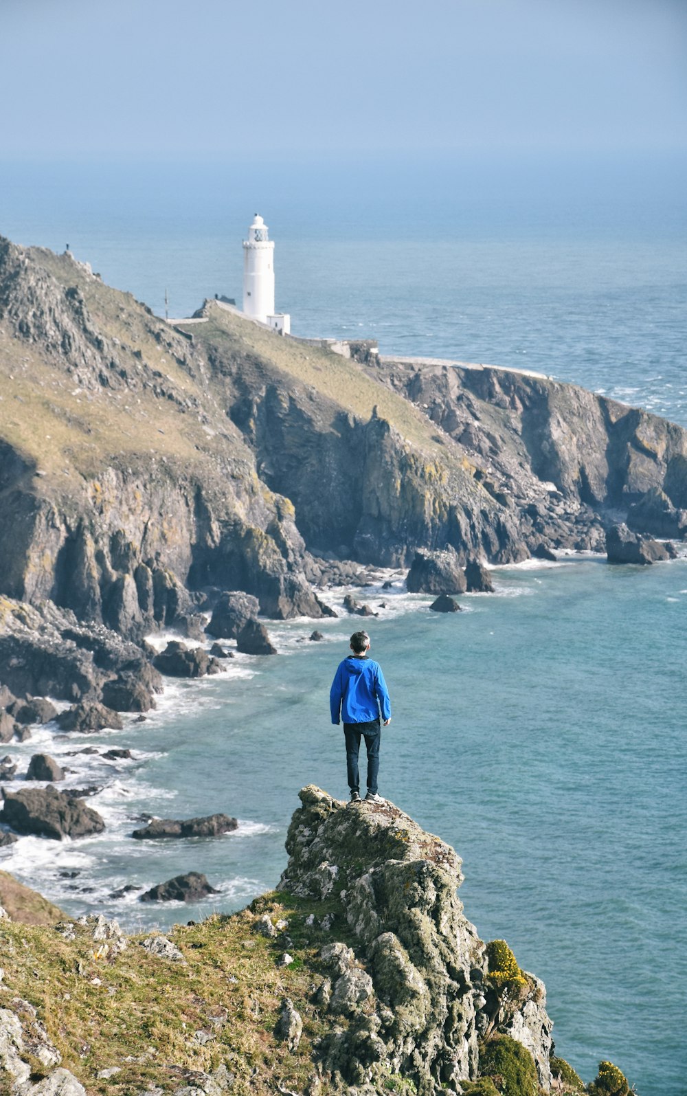Mann auf Felsen stehend mit Blick auf Leuchtturm und Meer