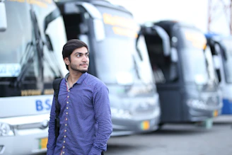 man in blue dress shirt standing in front of parked bus