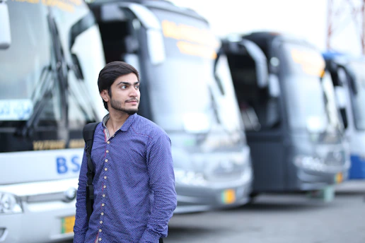 man in blue dress shirt standing in front of parked bus