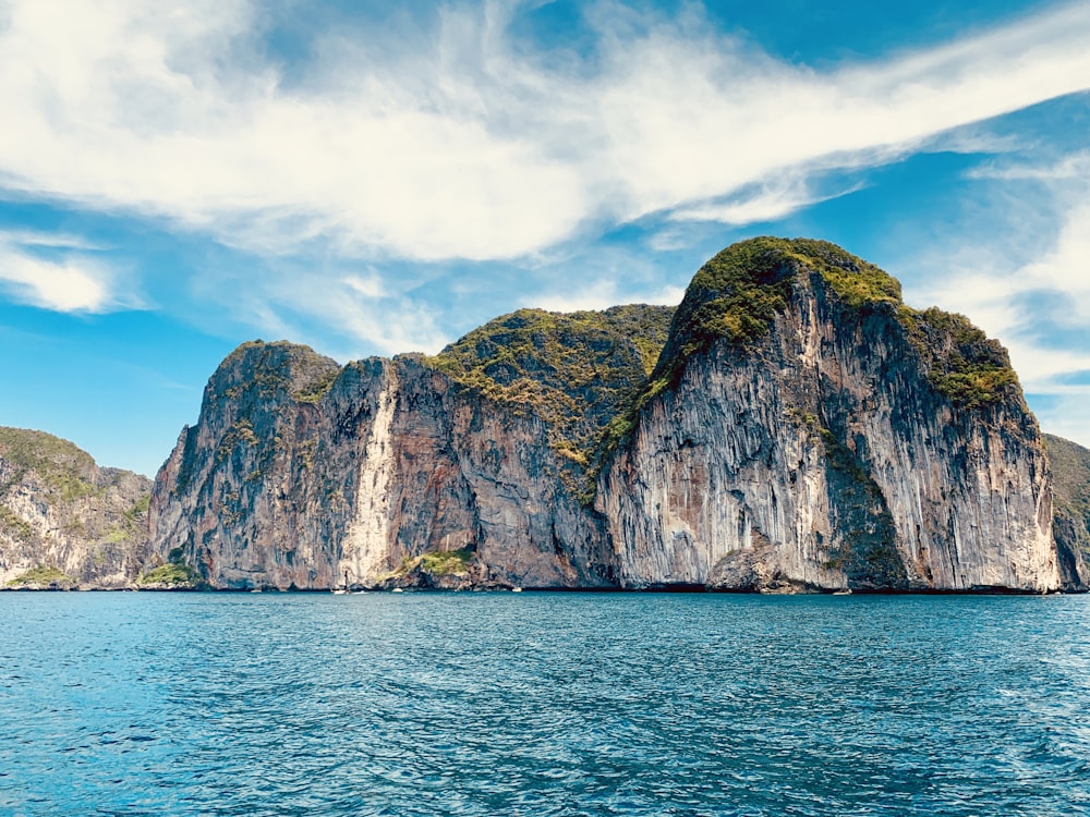 sea near rock mountain under blue sky and white clouds at daytime