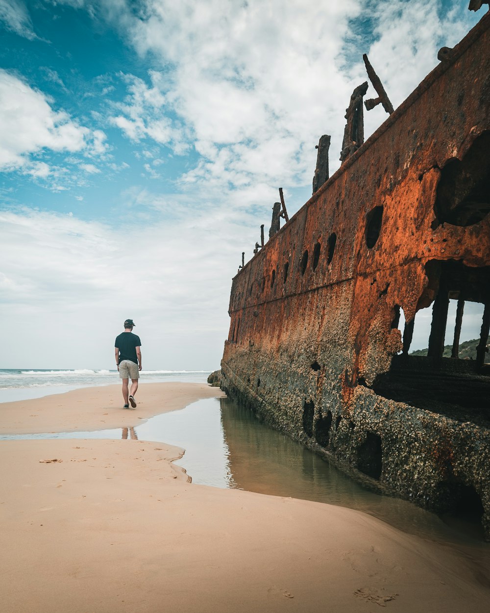 man standing near brown metal frame on seashore