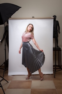 A model standing still in a softly lit studio wearing a reconstructed garment with sharp lines and muted tones.