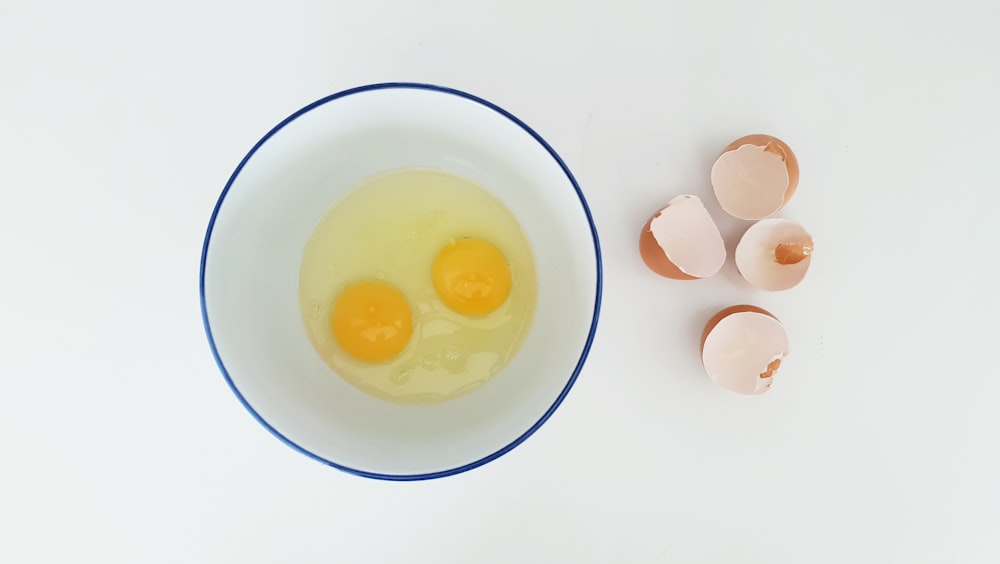 two cracked eggs in bowl beside egg sheels