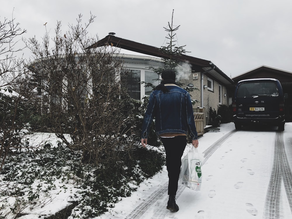 Mujer con bolsa de plástico caminando cerca de casa durante el invierno